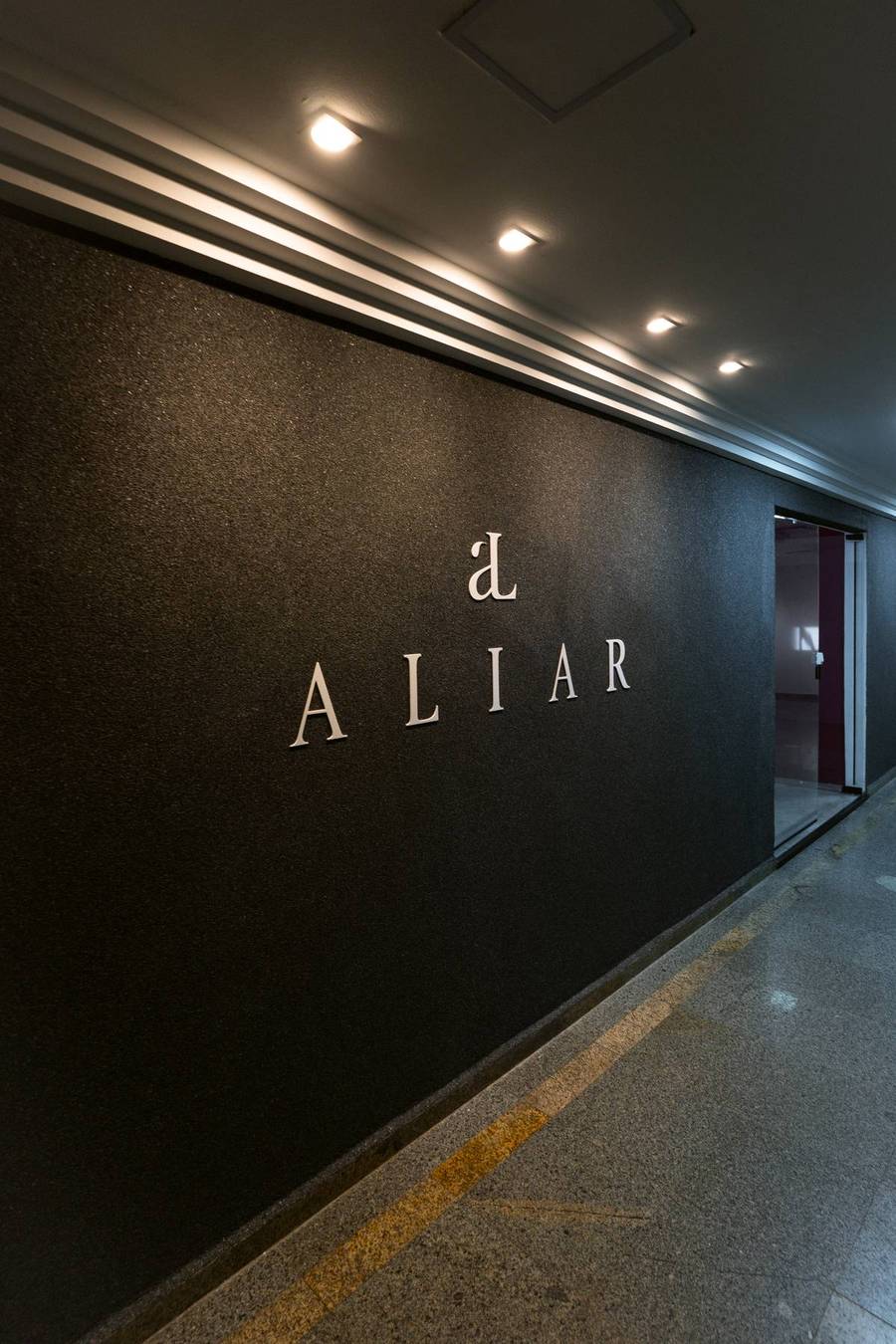 Entrada da Aliar Marketing no 17&ordm; andar do Edif&iacute;cio Aquarius Center, com o letreiro ALIAR em parede escura