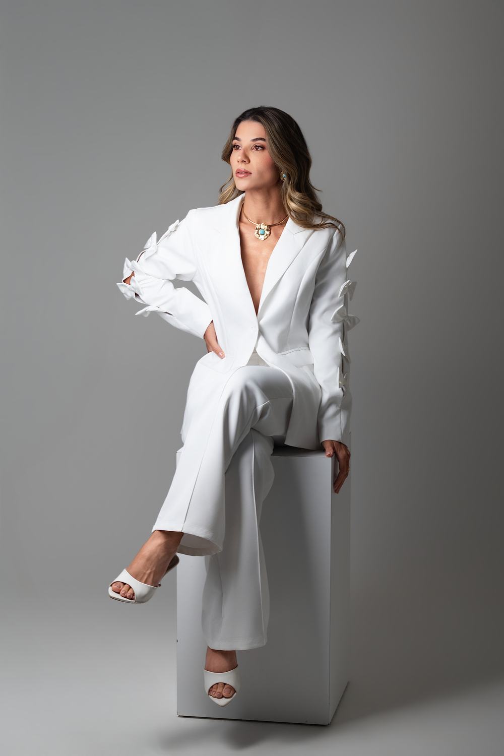 Ensaio de posicionamento: mulher de terno branco sentada em cubo, fundo claro de est&uacute;dio