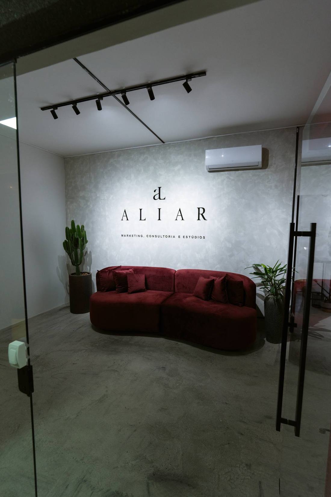 Recep&ccedil;&atilde;o da Aliar Marketing em Goi&acirc;nia, com sof&aacute; vinho e logotipo aplicado na parede