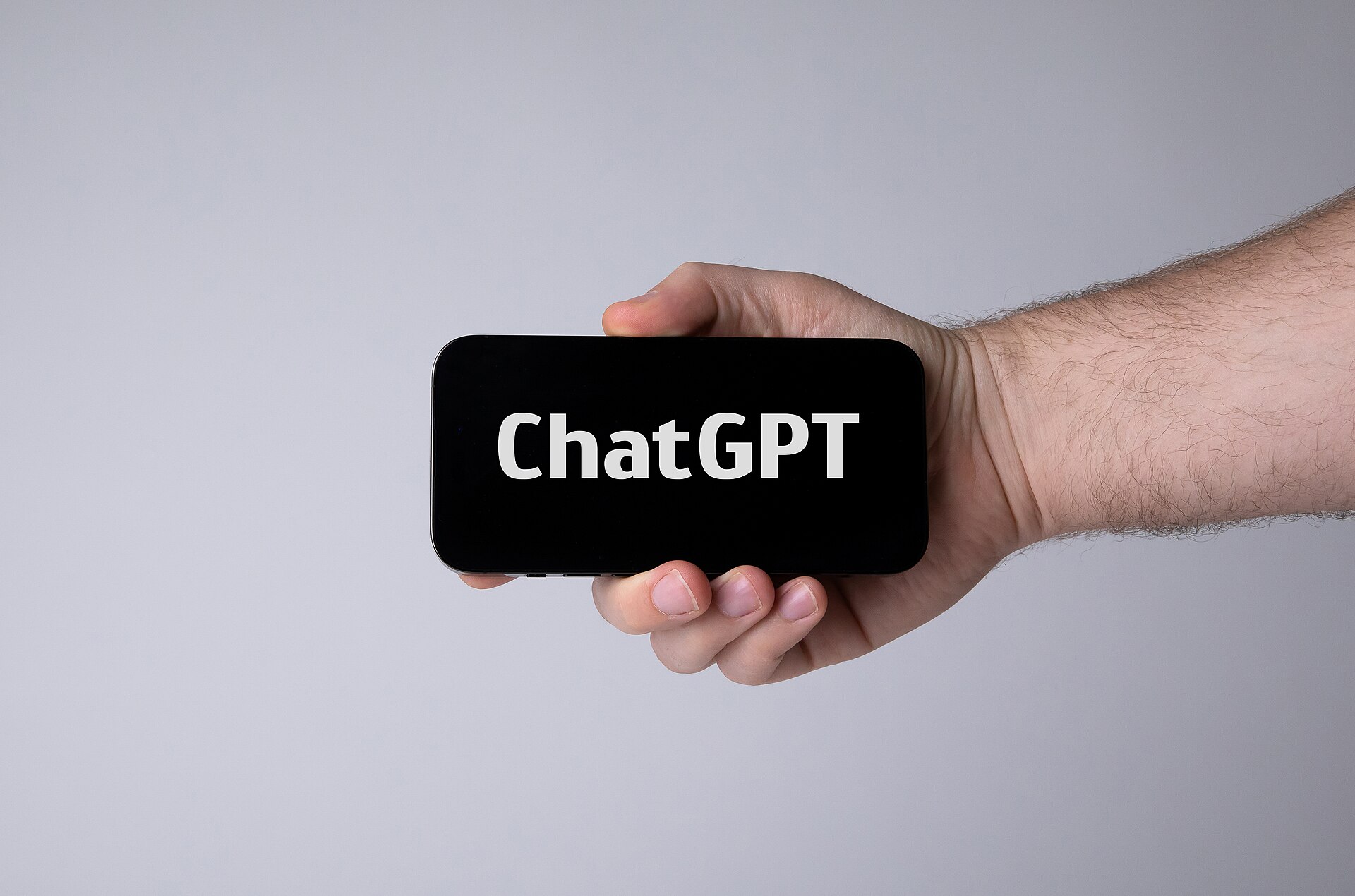Mão segurando um celular na horizontal, com a palavra ChatGPT na tela escura