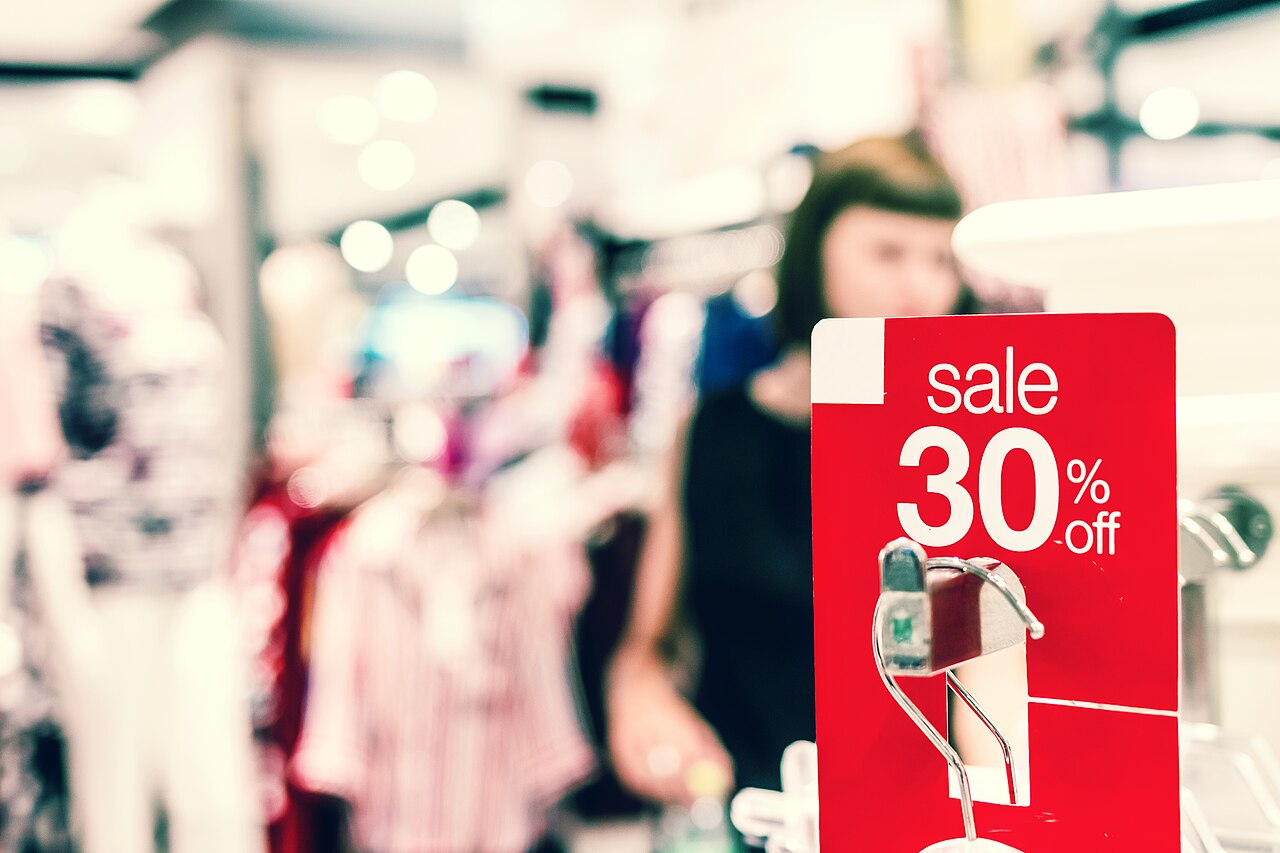 Placa vermelha de promoção com 30% de desconto em uma loja de roupas, com cliente ao fundo