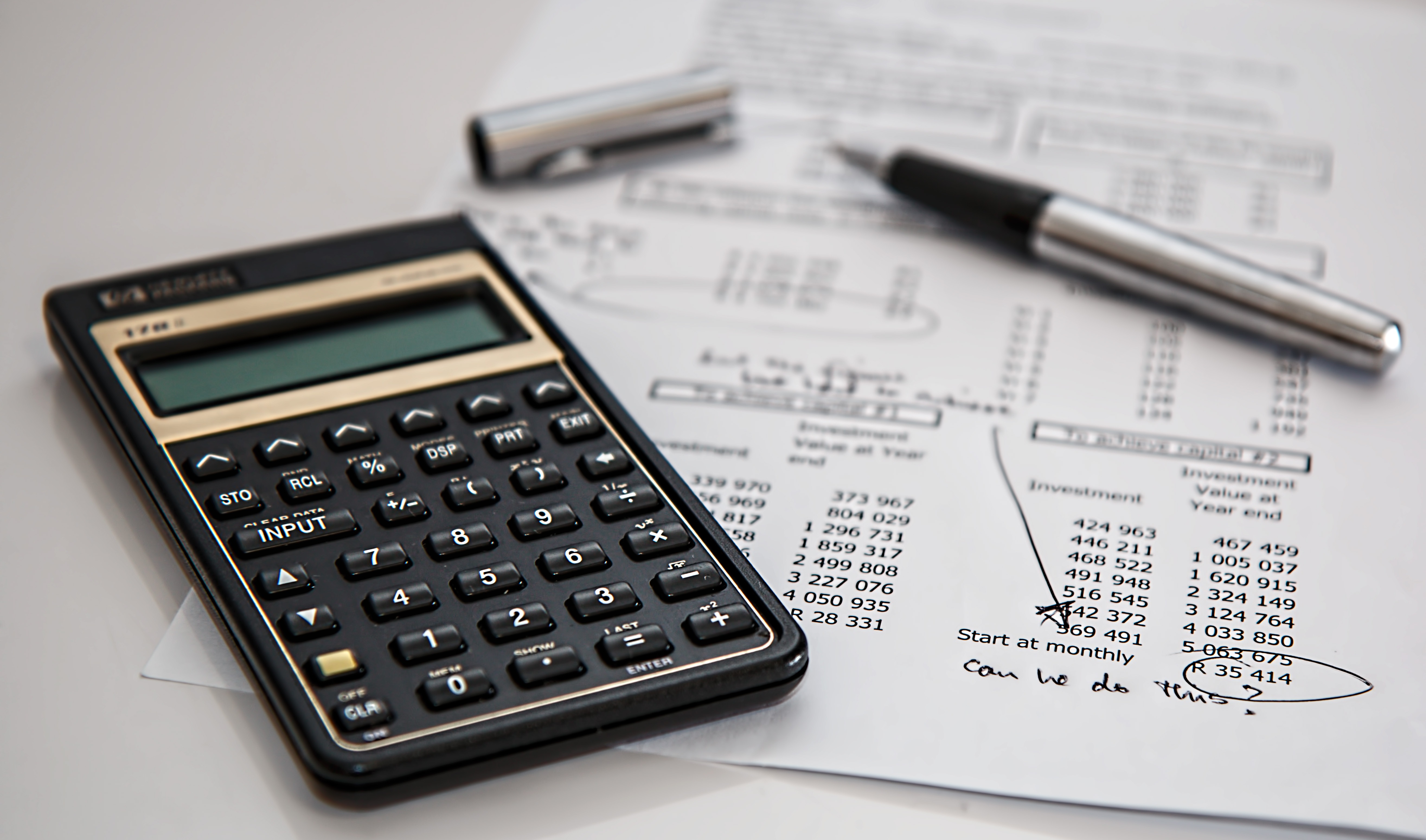 Calculadora sobre uma planilha de investimento, com uma caneta ao lado