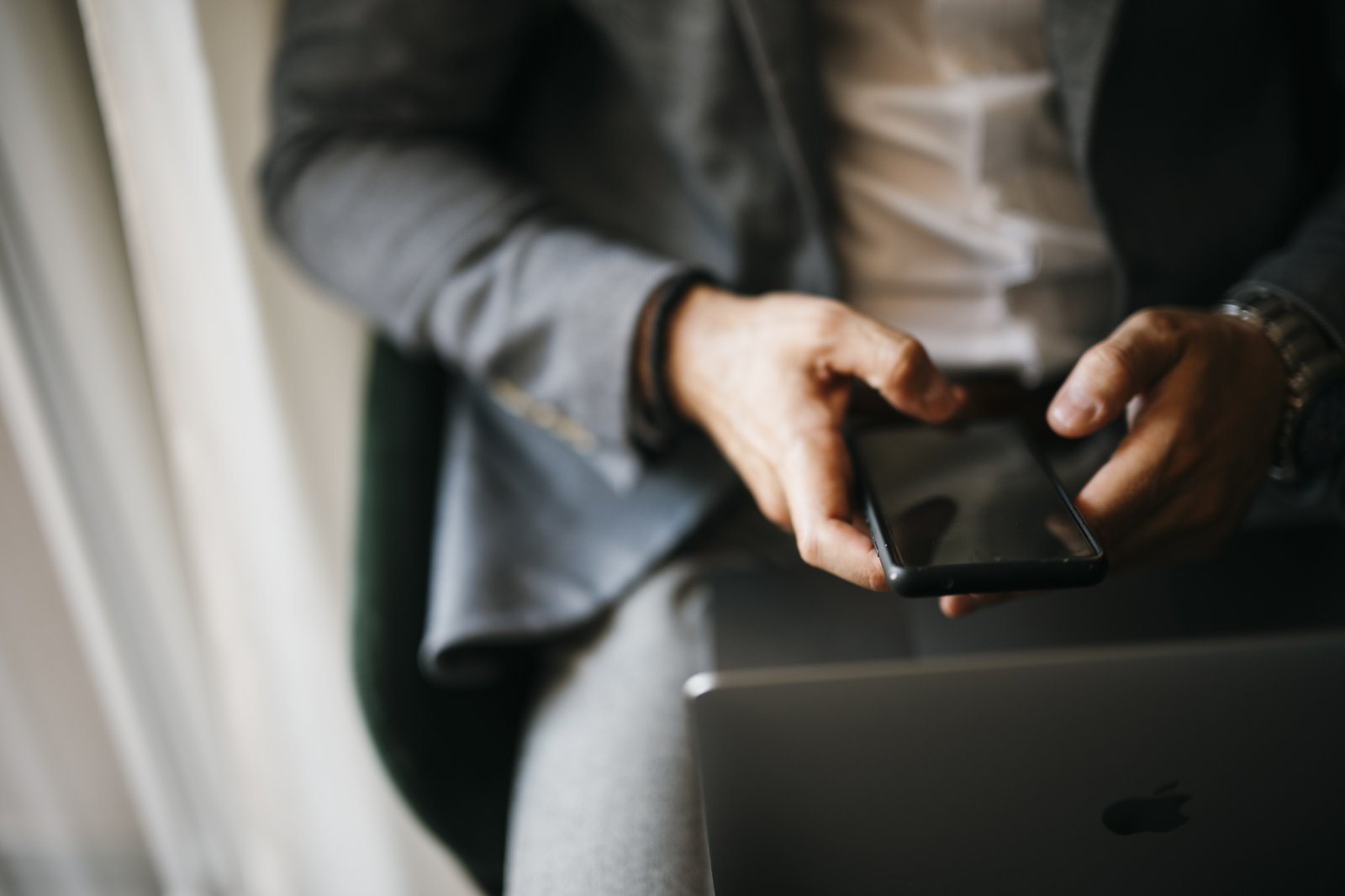 Empresário segurando o celular ao lado de um notebook, atendendo uma mensagem