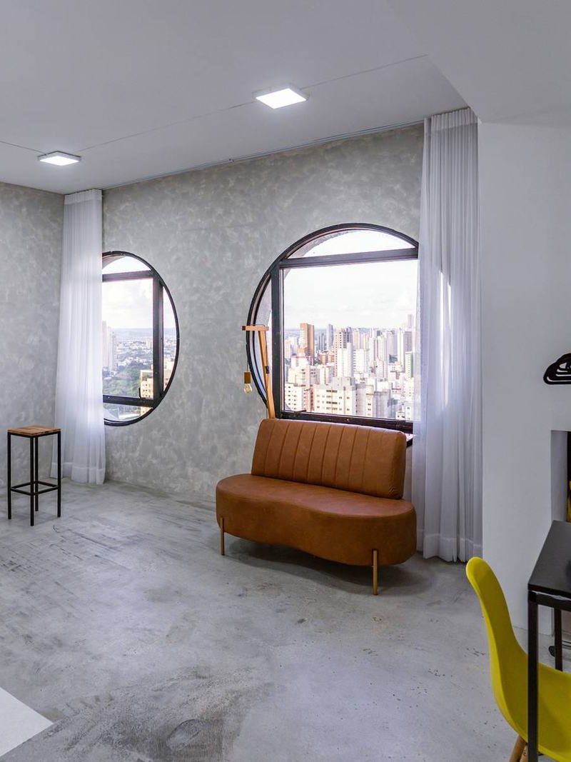 Lounge do Estúdio 2 da Aliar Estúdios, com sofá, janelas circulares e vista de Goiânia